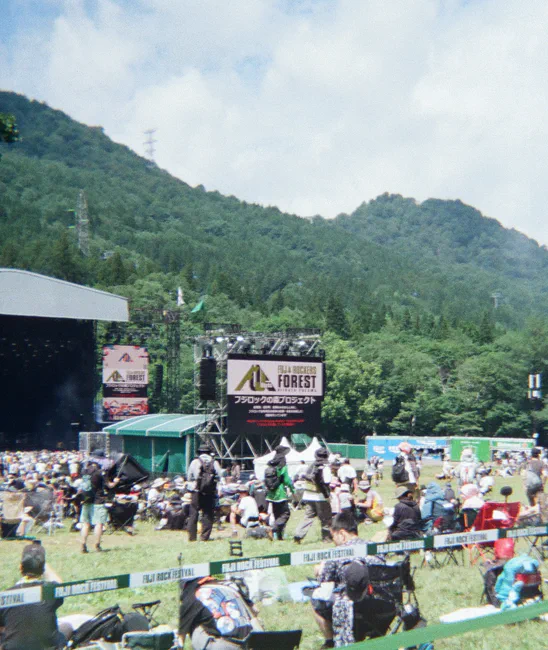 苗场的山脊与云层下，Fuji Rock 森林舞台前的草坡上散坐着观众。